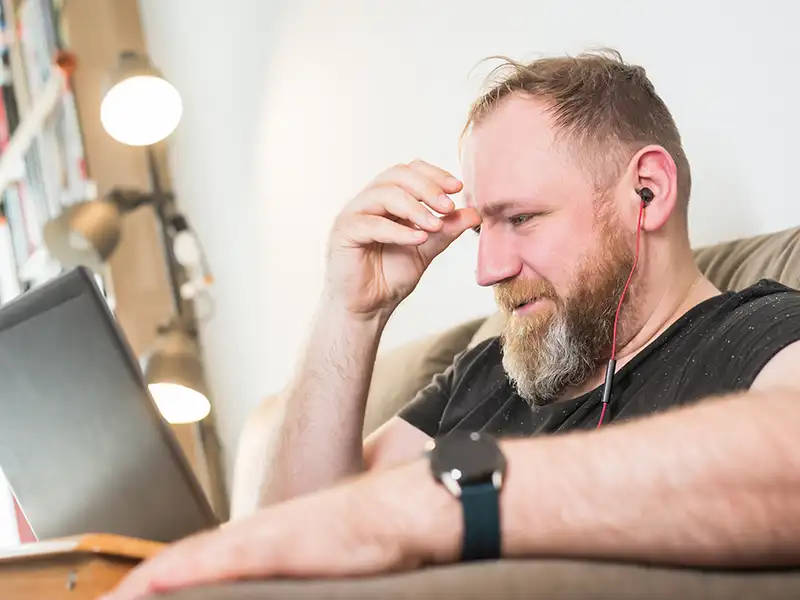 Guy sat on the sofa looking at his laptop
