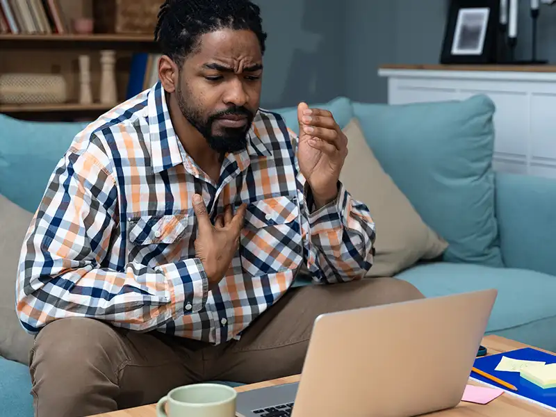 Man on the sofa with hi hand on his chest looking at his laptop