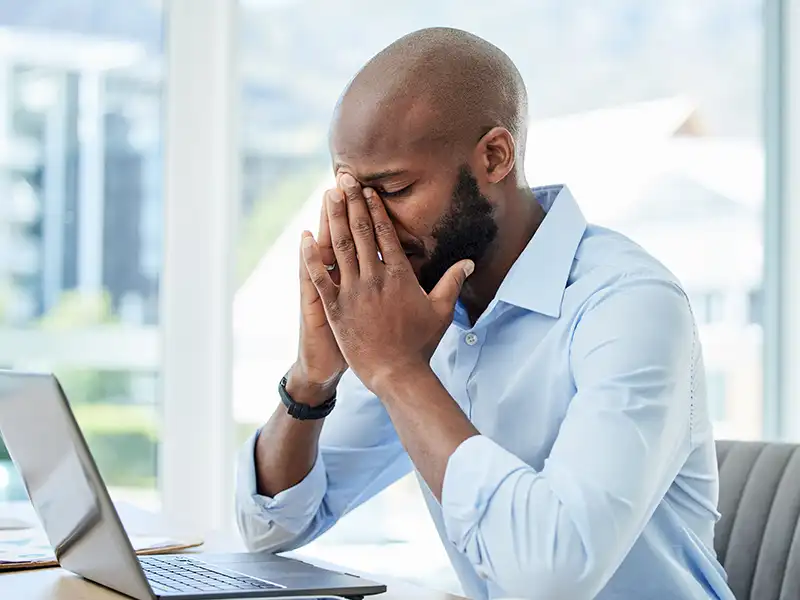 Office worker sat in front of a computer with his head in his hands