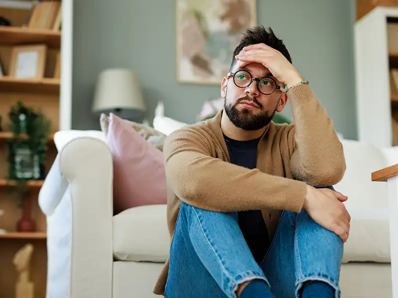 Young guy, sat on the floor of his home, clearly unsure what to do.