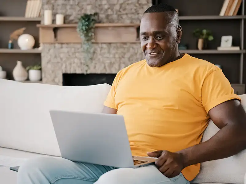 Man wearing an orange t-shirt, sat with his laptop on his knees