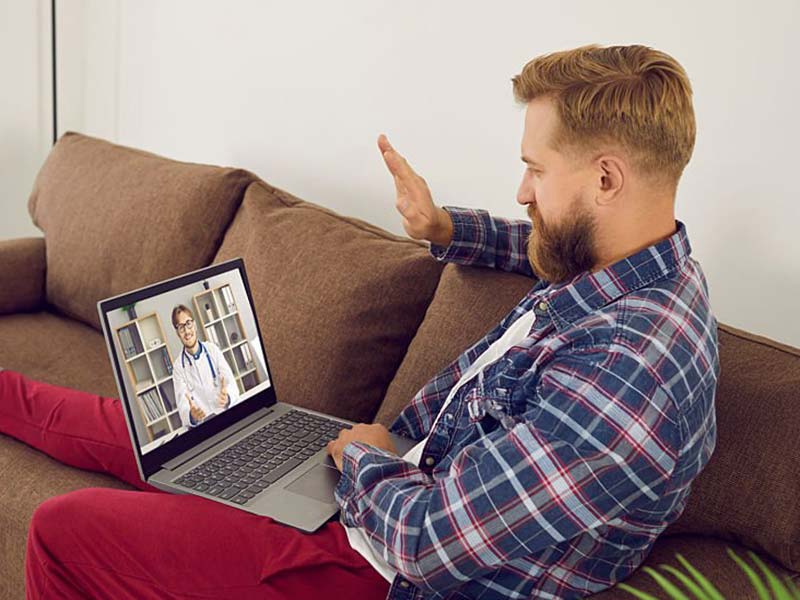Man on the sofa with hi hand on his chest looking at his laptop