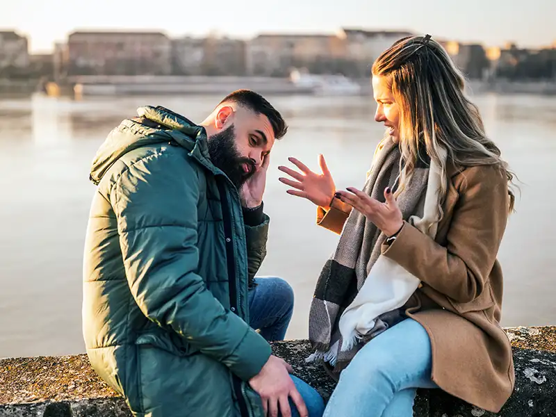 A man and his partner, on the side of a river, having a heated discussion